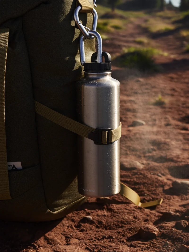 Edelstahl-Trinkflasche mit Karabiner am Rucksackgurt, Morgentau auf dem Bergpfad