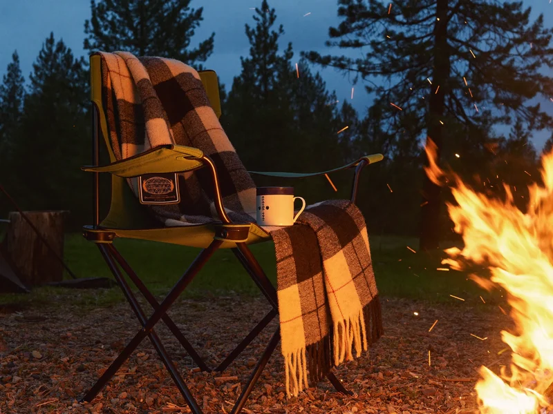 Campingabend am Lagerfeuer mit Klappstuhl, Wolldecke und emailliertem Becher